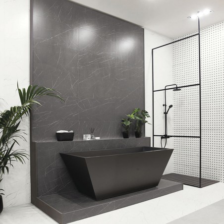Una elegante y moderna bañera de color gris oscuro descansa contra una pared decorativa a juego. El ambiente circundante present Una elegante y moderna bañera de color gris oscuro descansa contra una pared decorativa a juego. El ambiente circundante present