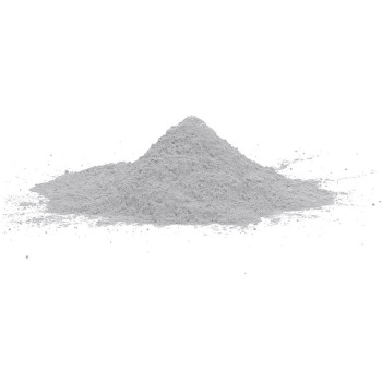 Un petit tas de poudre grise repose sur un fond blanc uni, suggérant un contexte de laboratoire ou de matériau de construction.