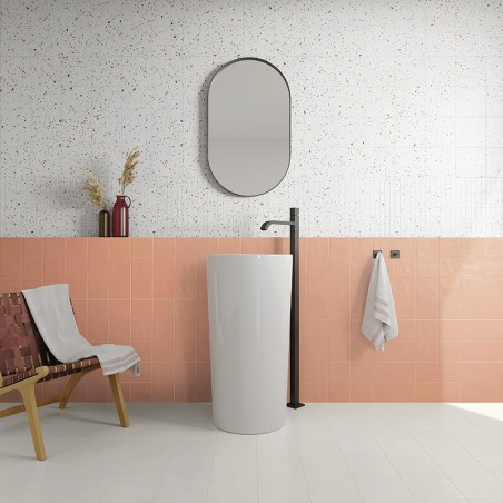 Un grand lavabo cylindrique blanc et un robinet noir se dressent dans une salle de bains ornée de carrelage rose et moucheté, au