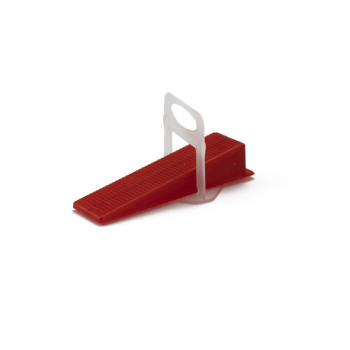 Un petit coin en plastique rouge à texture striée se trouve sur un fond blanc uni.