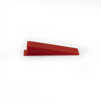 Een rode plastic wig rust op een effen wit oppervlak. Het heeft een geribbelde textuur langs de schuine zijde.