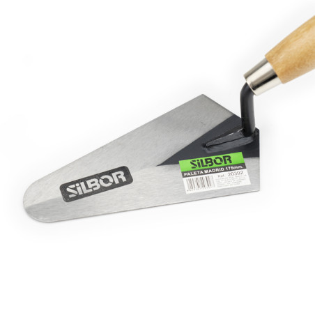 A metal trowel with a wooden handle lies on a white surface. It has a triangular blade, labeled with `SILBOR` and a green sticke