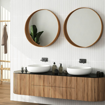 Dos espejos redondos que reflejan la luz cuelgan sobre un moderno tocador con textura de madera. Los lavabos blancos y los dispe