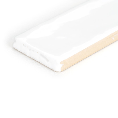 Un carreau de céramique rectangulaire blanc brillant repose sur le côté, avec un bord beige apparent, sur un fond blanc uni.