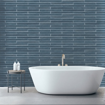Una bañera independiente blanca se encuentra sobre un piso claro, debajo de una pared con azulejos de color azul oscuro. Cerca h