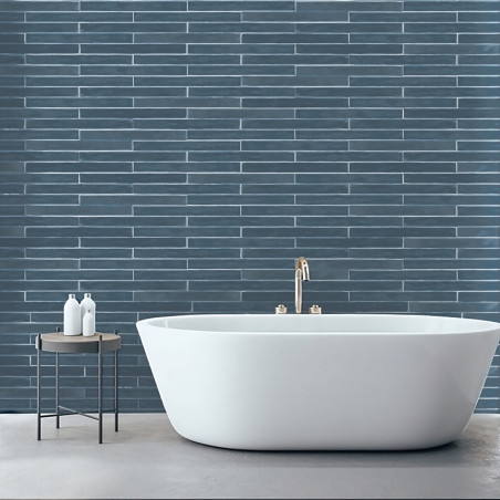 Una bañera independiente blanca se encuentra sobre un piso claro, debajo de una pared con azulejos de color azul oscuro. Cerca h