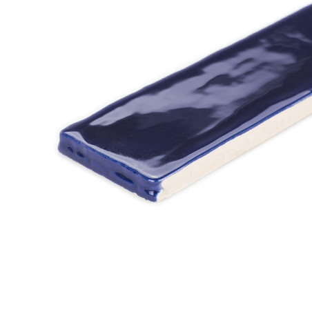 Un azulejo rectangular revestido con un esmalte azul oscuro brillante descansa sobre una superficie blanca, mostrando su acabado