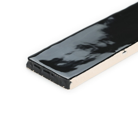 Se muestra parcialmente Un azulejo cerámico rectangular, con un esmalte negro brillante en su superficie, sobre un fondo blanco 