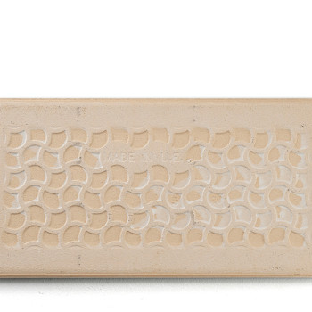 Un azulejo beige rectangular muestra un patrón repetitivo de semicírculos entrelazados. En el centro, un texto tenue dice: `MADE