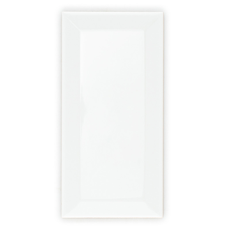 A glossy, rectangular white tile with beveled edges rests on a plain white background, reflecting soft ambient light.