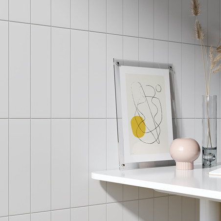 Un dessin au trait abstrait encadré avec un cercle jaune repose sur un rebord blanc contre des murs carrelés, à côté d'un vase r Un dessin au trait abstrait encadré avec un cercle jaune repose sur un rebord blanc contre des murs carrelés, à côté d'un vase r