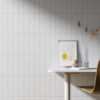 Een wit betegelde muur vormt een strak decor voor een minimalistische werkruimte, met een ingelijste abstracte tekening, een vaa