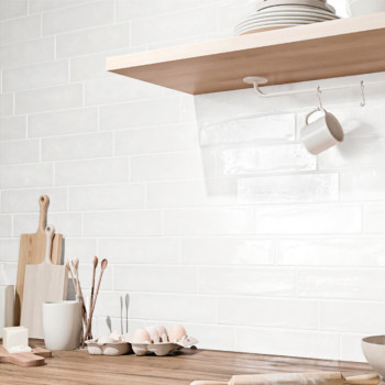 White rectangular tiles form a backsplash, reflecting light. Wooden shelves hold dishes, while eggs and utensils rest on the cou