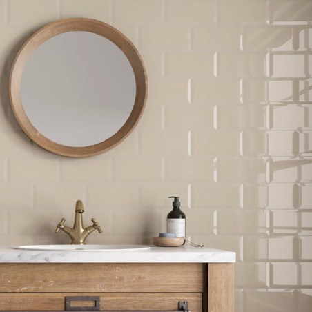Un espejo redondo cuelga sobre una pared de azulejos beige. El tocador de madera sostiene un lavabo de mármol con grifo de latón