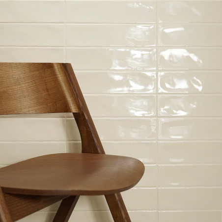 Een houten stoel staat schuin tegen een glanzende, crèmekleurige tegelwand en reflecteert licht, in een minimalistische binnenom Een houten stoel staat schuin tegen een glanzende, crèmekleurige tegelwand en reflecteert licht, in een minimalistische binnenom