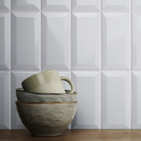 Una pila de cuencos de cerámica y una taza se encuentran sobre una superficie de madera, frente a azulejos blancos brillantes co