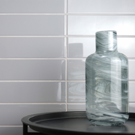Una botella de vidrio arremolinada descansa sobre una bandeja negra, colocada contra una pared de azulejos blancos brillantes de