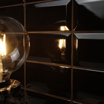 A glowing light bulb emits warm light, reflected on glossy black, rectangular tiles. The setup creates a sleek, modern ambiance.