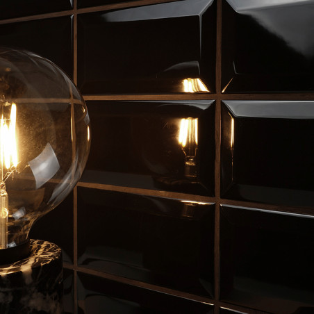 Una bombilla incandescente emite una luz cálida que se refleja en azulejos rectangulares de color negro brillante. La configurac Una bombilla incandescente emite una luz cálida que se refleja en azulejos rectangulares de color negro brillante. La configurac