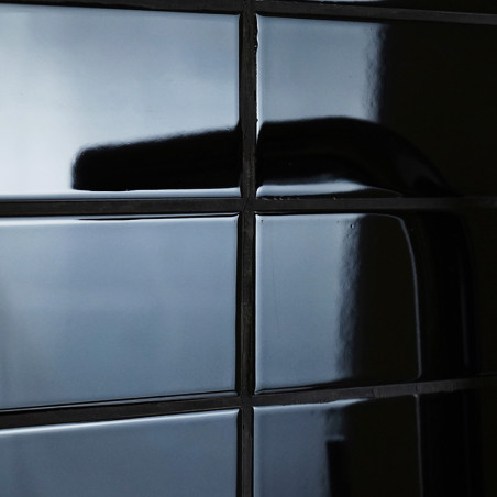 azulejos de cerámica negras y brillantes que reflejan la luz forman un patrón de cuadrícula. Una sombra se curva a lo largo de u azulejos de cerámica negras y brillantes que reflejan la luz forman un patrón de cuadrícula. Una sombra se curva a lo largo de u