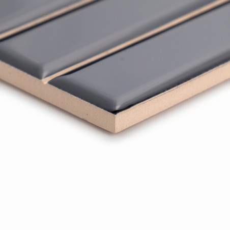 Un azulejo rectangular con tiras elevadas de color gris oscuro brillante se asienta sobre una superficie beige, resaltando su di