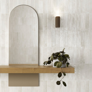 Un miroir arqué repose au-dessus d’une étagère en bois, accompagné d’une plante luxuriante et rampante. Une applique murale cyli