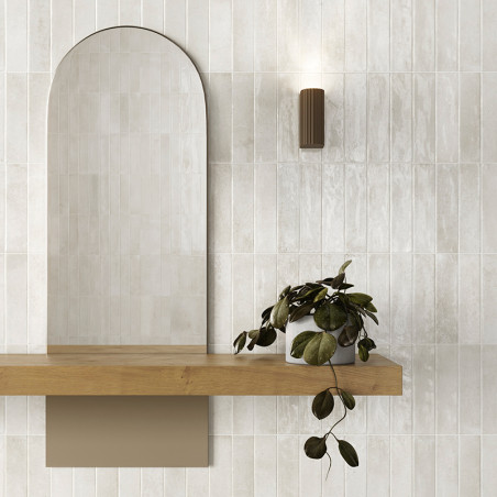 Een gebogen spiegel rust boven een houten plank, vergezeld van een weelderige, hangende plant. Een moderne, cilindrische wandkan