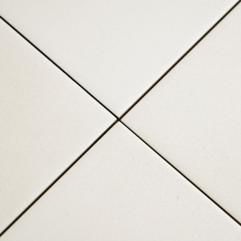 Cuatro azulejos de cerámica blanca se unen en un punto central, formando una forma más con líneas estrechas de lechada, colocada
