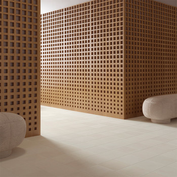 Uma parede de grade de madeira divide uma sala adornada com piso bege, acompanhado por pufes cinza arredondados. O espaço parece