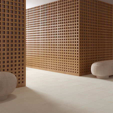 Una pared de rejilla de madera divide una habitación adornada con azulejos de color beige, acompañadas de otomanas grises redond