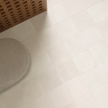 Um piso de azulejos bege claro se estende por toda a área. Um pufe redondo de tecido bege fica em um canto ao lado de um painel 