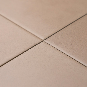 Quatre carreaux beiges se croisent parfaitement, formant une petite croix à leurs coins. Ils sont placés sur une surface plane e