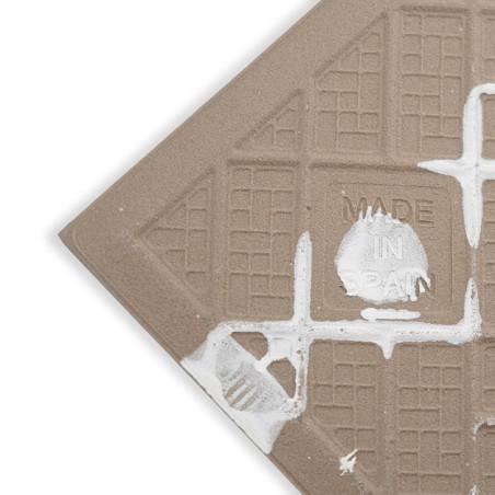 A textured ceramic tile with grid patterns features white splashes. Embossed text reads `MADE IN SPAIN` near the center.