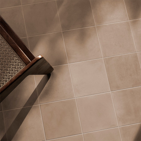 A wooden chair casts a shadow on light brown, square ceramic tiles, creating a warm and calm ambiance in the room.