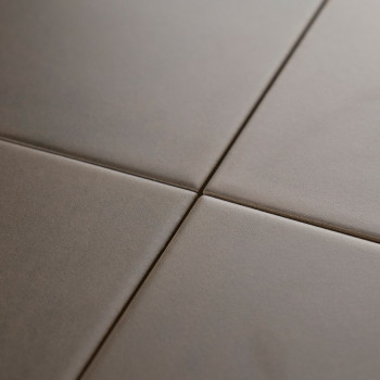 Quatre carreaux carrés lisses et mats se rejoignent sur une ligne de coulis centrale, formant un motif de grille minimal sur une