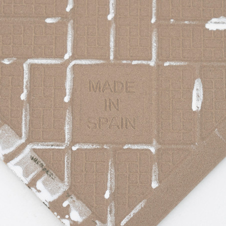 Un azulejo cerámico texturizado muestra las palabras `MADE IN SPAIN` grabadas en el centro, con un patrón de cuadrícula y restos Un azulejo cerámico texturizado muestra las palabras `MADE IN SPAIN` grabadas en el centro, con un patrón de cuadrícula y restos
