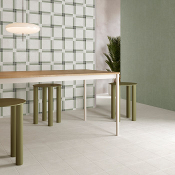 A modern dining room table sits on light square tiles, surrounded by green cylindrical stools. A plaid-patterned wall and plant 