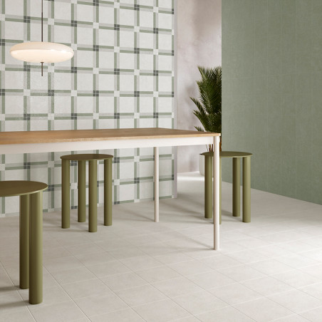 Uma moderna mesa de jantar fica sobre azulejos quadrados claros, cercada por bancos cilíndricos verdes. Uma parede e uma planta 