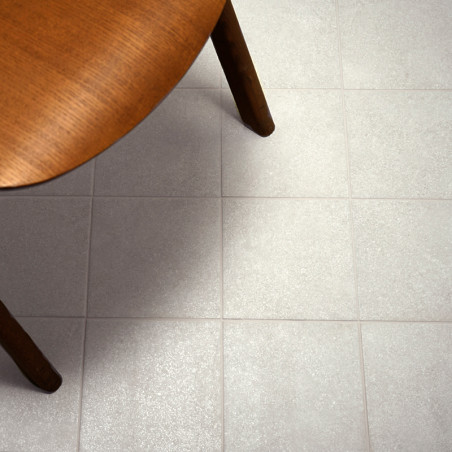 A round wooden table partially covers a grid of light gray floor tiles, creating a warm and minimalist interior setting.