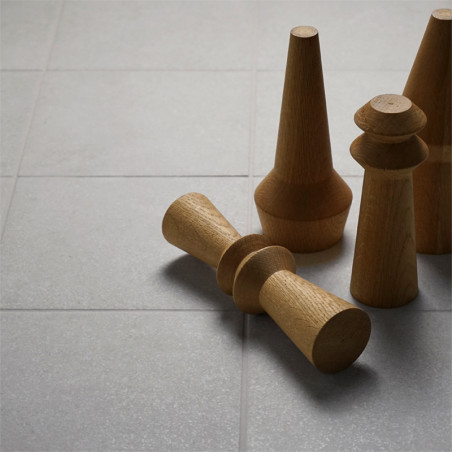 Des pièces d'échecs en bois sont éparpillées sur une surface carrelée gris clair, une pièce étant renversée. La scène est calme 