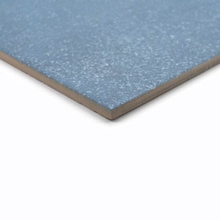 Eine blaue Keramikfliese, die flach aufliegt, weist auf ihrer glatten Oberfläche eine gesprenkelte Textur vor einem schlichten w
