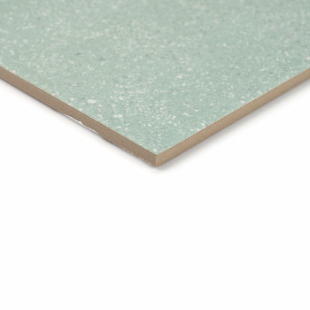 Un carreau de céramique moucheté de vert se trouve sur un fond blanc, montrant sa surface lisse et polie et ses bords inclinés p