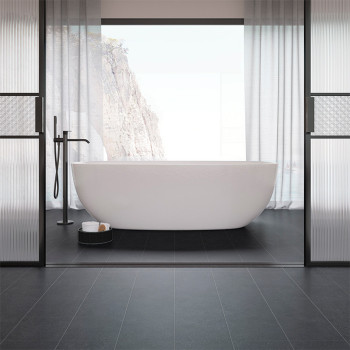Eine weiße freistehende Badewanne steht in der Mitte eines minimalistischen Badezimmers mit schwarzen Fliesen, eingerahmt von gr