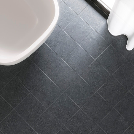 Dark gray square tiles form a grid pattern on a bathroom floor next to a white bathtub and sheer white curtain by a window.