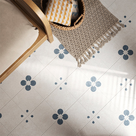 Un azulejo de color gris claro presenta motivos florales azules, creando un patrón simétrico. Está al lado de una silla de mimbr Un azulejo de color gris claro presenta motivos florales azules, creando un patrón simétrico. Está al lado de una silla de mimbr