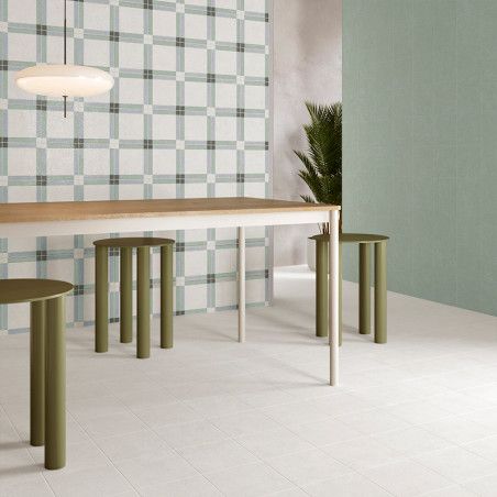 Uma sala minimalista apresenta uma mesa de madeira com bancos cilíndricos verdes embaixo dela. Uma parede com estampa xadrez com