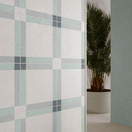 A tiled wall shows a plaid pattern in soft gray, green, and blue, placed indoors beside a potted palm plant in a minimalist room