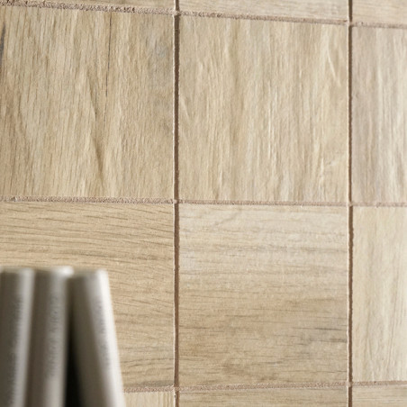 Fliesen mit hellem Holzmaserungsmuster im Raster angeordnet. Im Vordergrund sind unscharfe zylindrische Objekte zu sehen, möglic