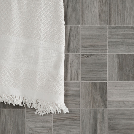 Uma toalha branca texturizada está pendurada sobre uma grade de pequenos ladrilhos quadrados cinza com um padrão semelhante a ma Uma toalha branca texturizada está pendurada sobre uma grade de pequenos ladrilhos quadrados cinza com um padrão semelhante a ma