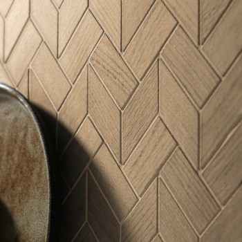 Les carreaux de céramique beige s'emboîtent dans un motif à chevrons, créant une toile de fond murale texturée. Au premier plan,